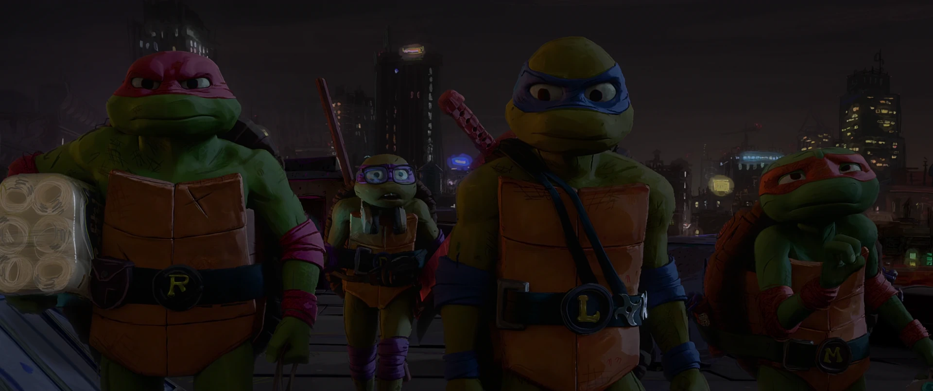 All four Turtles stand in a line on a rooftop at night, facing forward with the lit NYC skyline behind them.