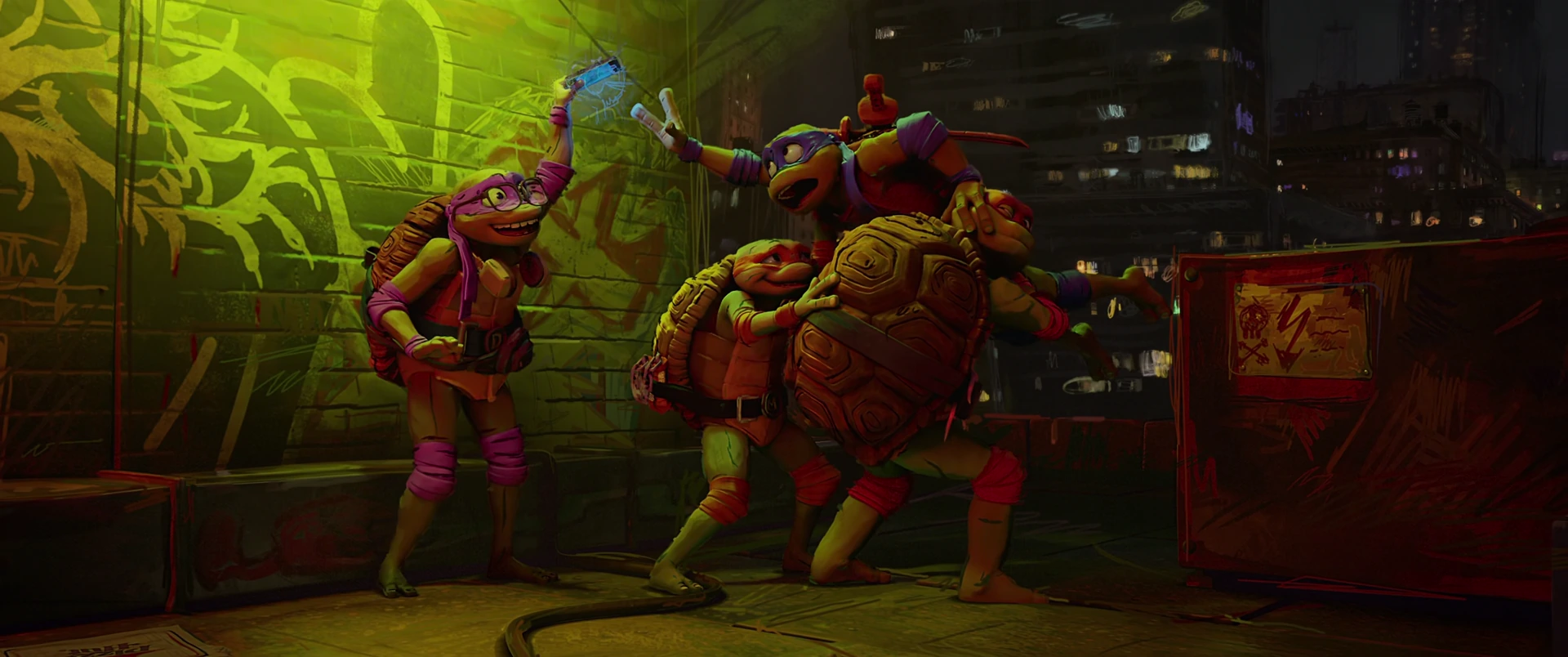 Donatello raises an object in celebration while Raphael cheers beside him, fists up against a graffiti wall at night.