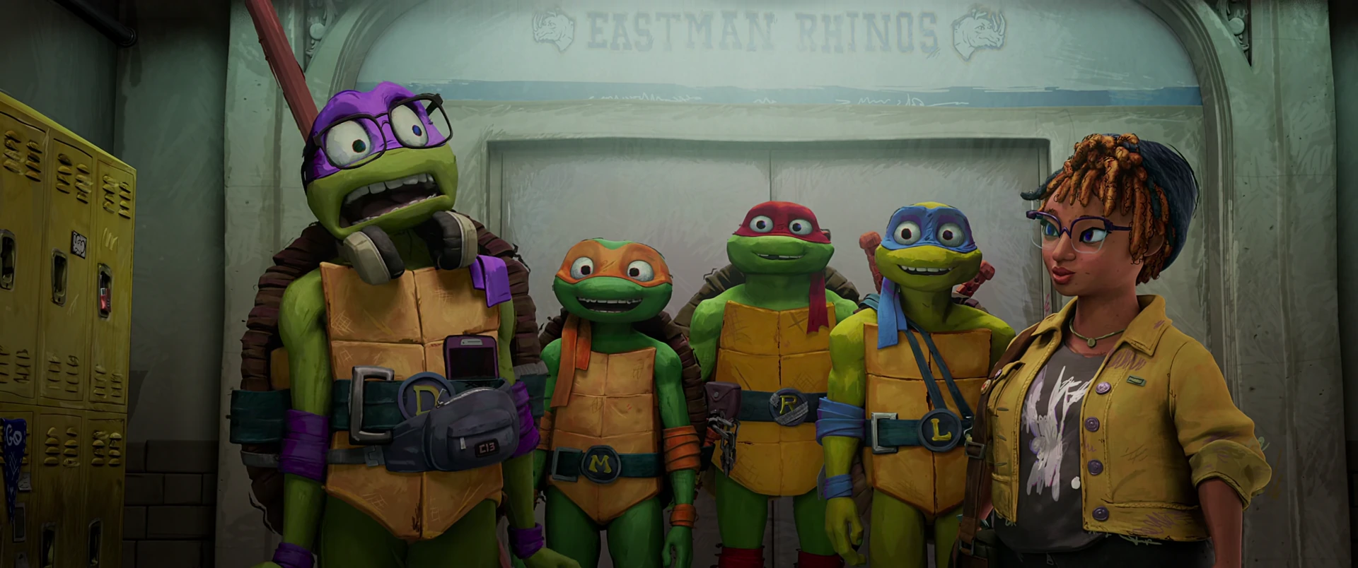 Donatello leans forward with a wide grin beside his brothers and April against the school’s yellow locker bank.