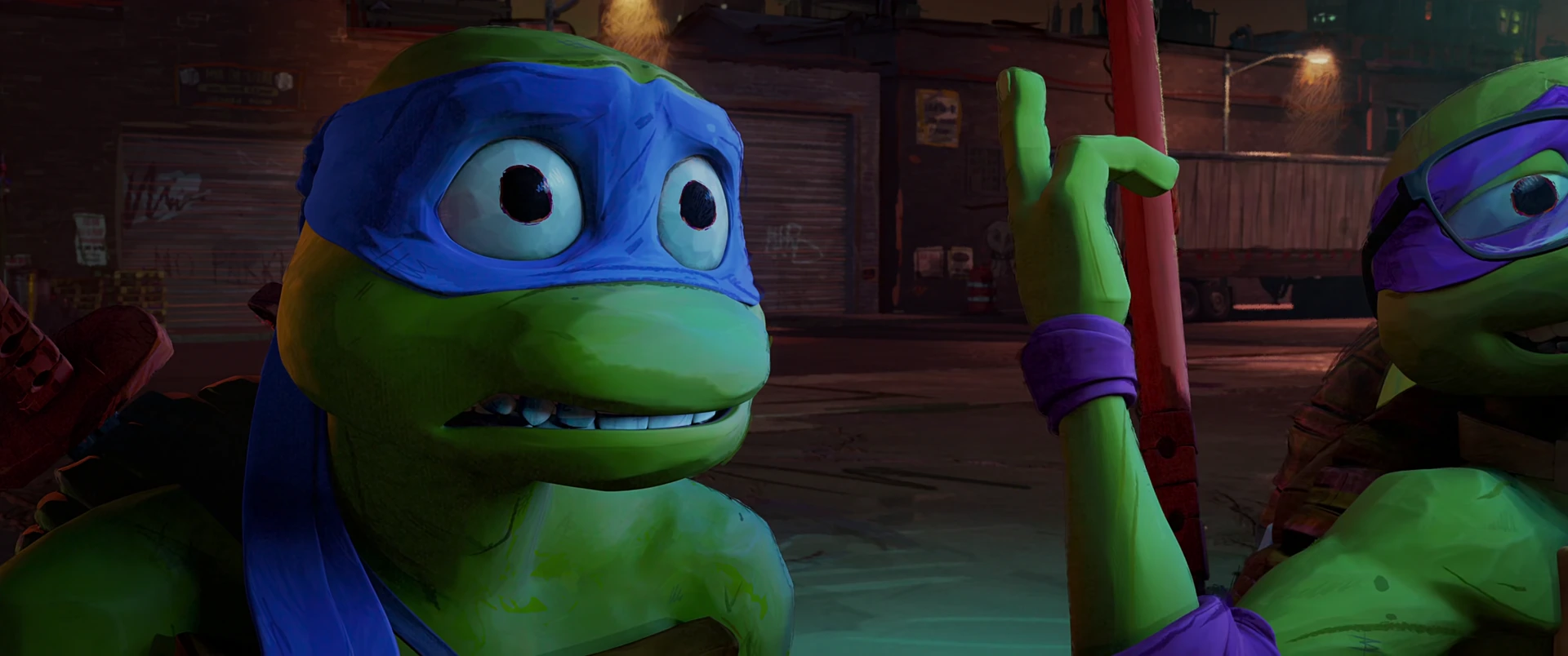 Leo in blue mask raises a finger mid-explanation while Donnie peers in from the right, lit by warm urban glow.