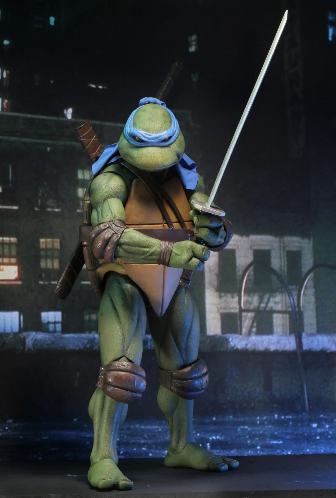 NECA's quarter scale 1990 movie Leonardo, drawing a katana on a rooftop backdrop of lit windows and a puddled roof.