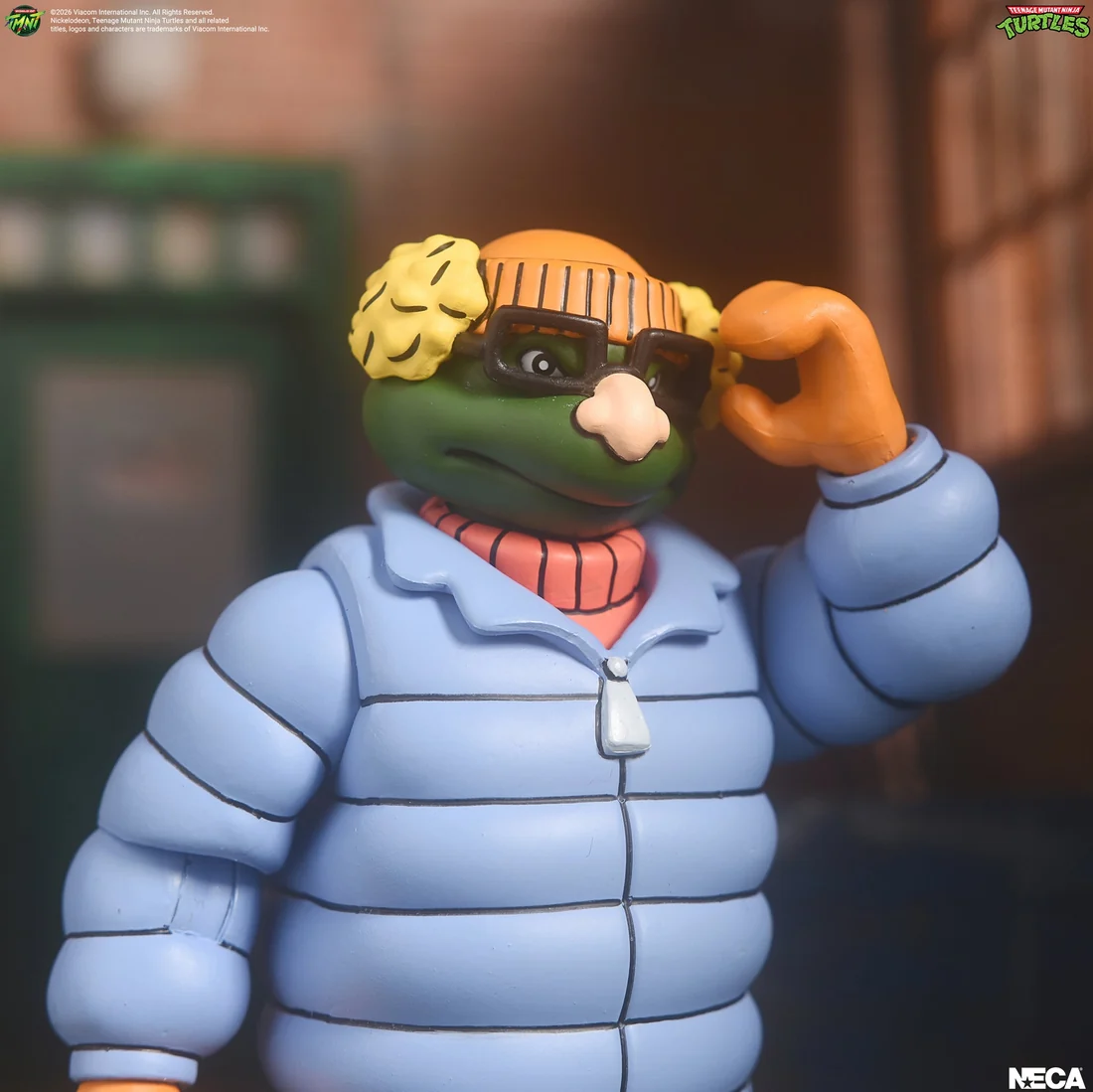 Incognito Mikey in a blue puffer jacket, orange beanie and blonde wig, lifting the false nose and glasses away from his face.