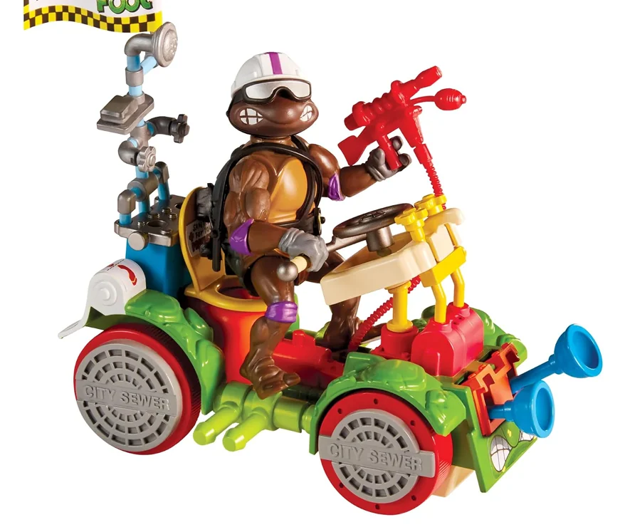 The Toilet Taxi with Donatello at the wheel in a crash helmet and goggles, on manhole cover wheels with a red bowl blaster and blue horns